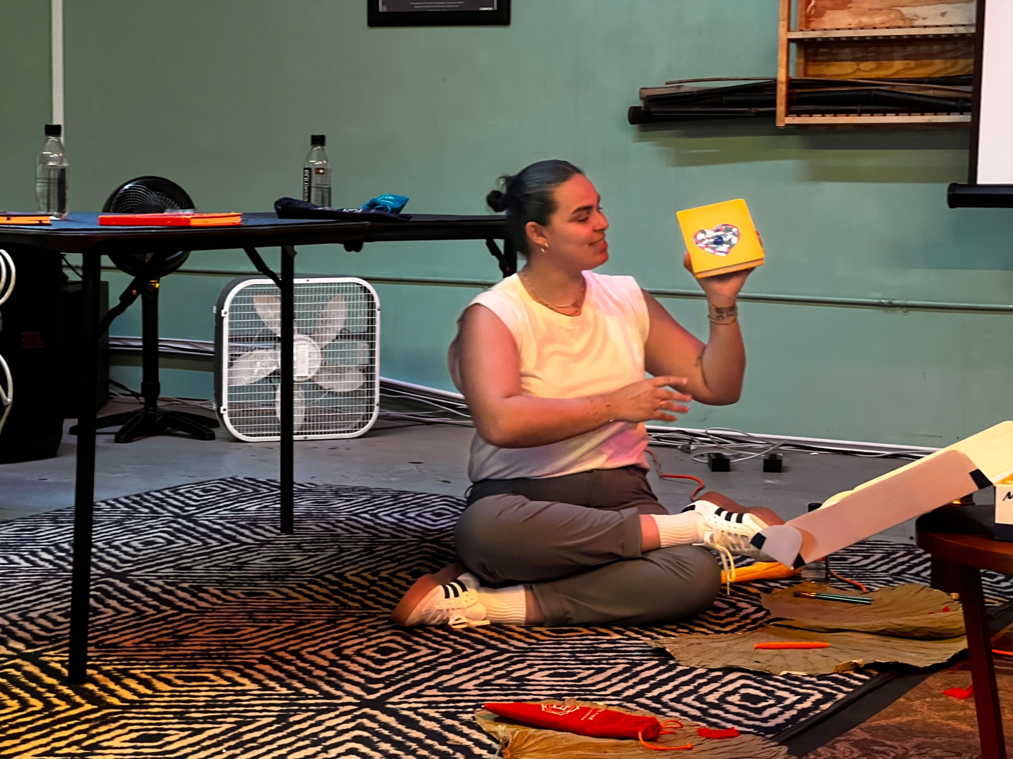 A participant seated on the floor holding and discussing a colorful object she created